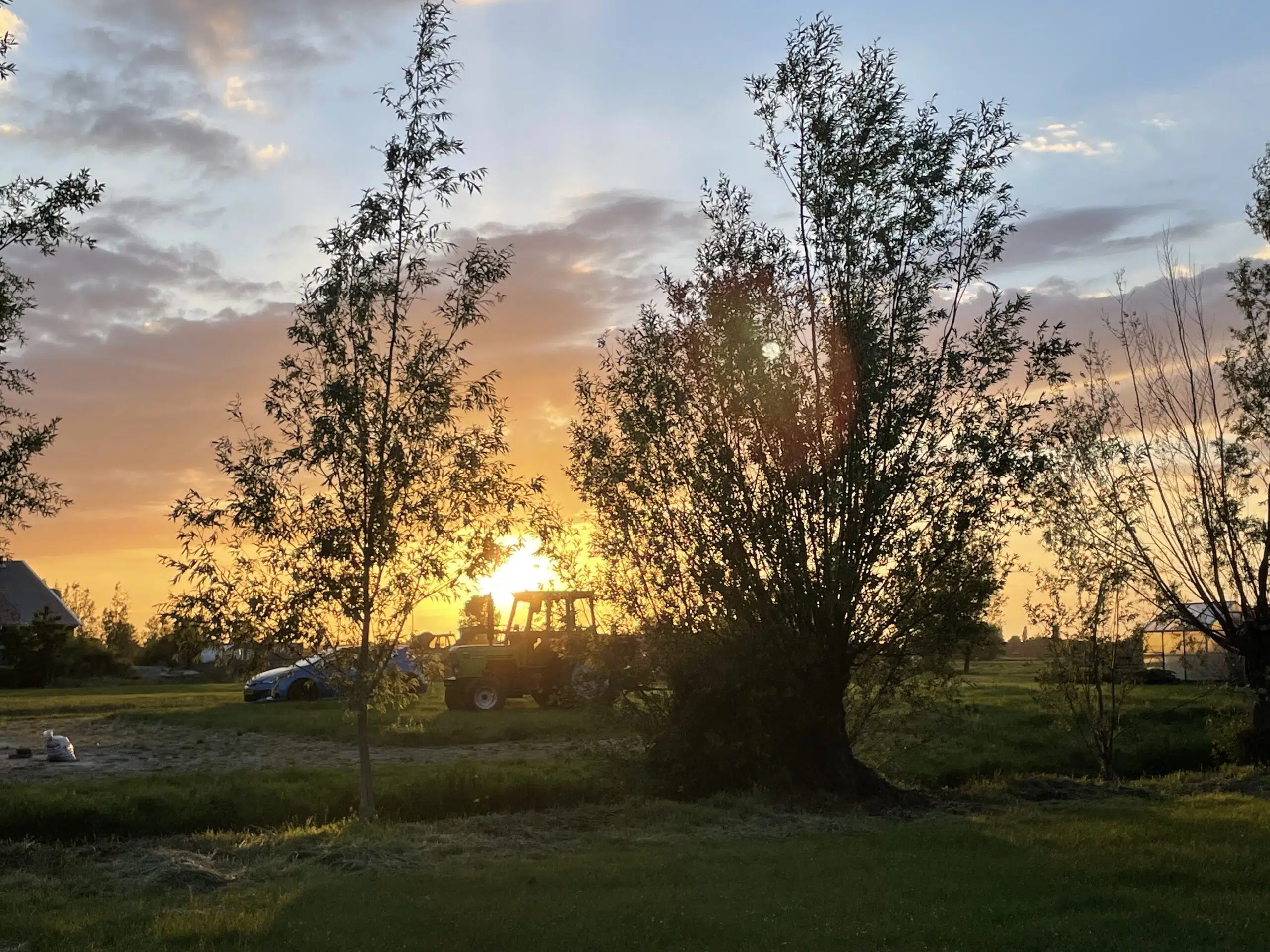 foto van de weilanden met een groene traktor en tegenlicht van de ondergaande zon