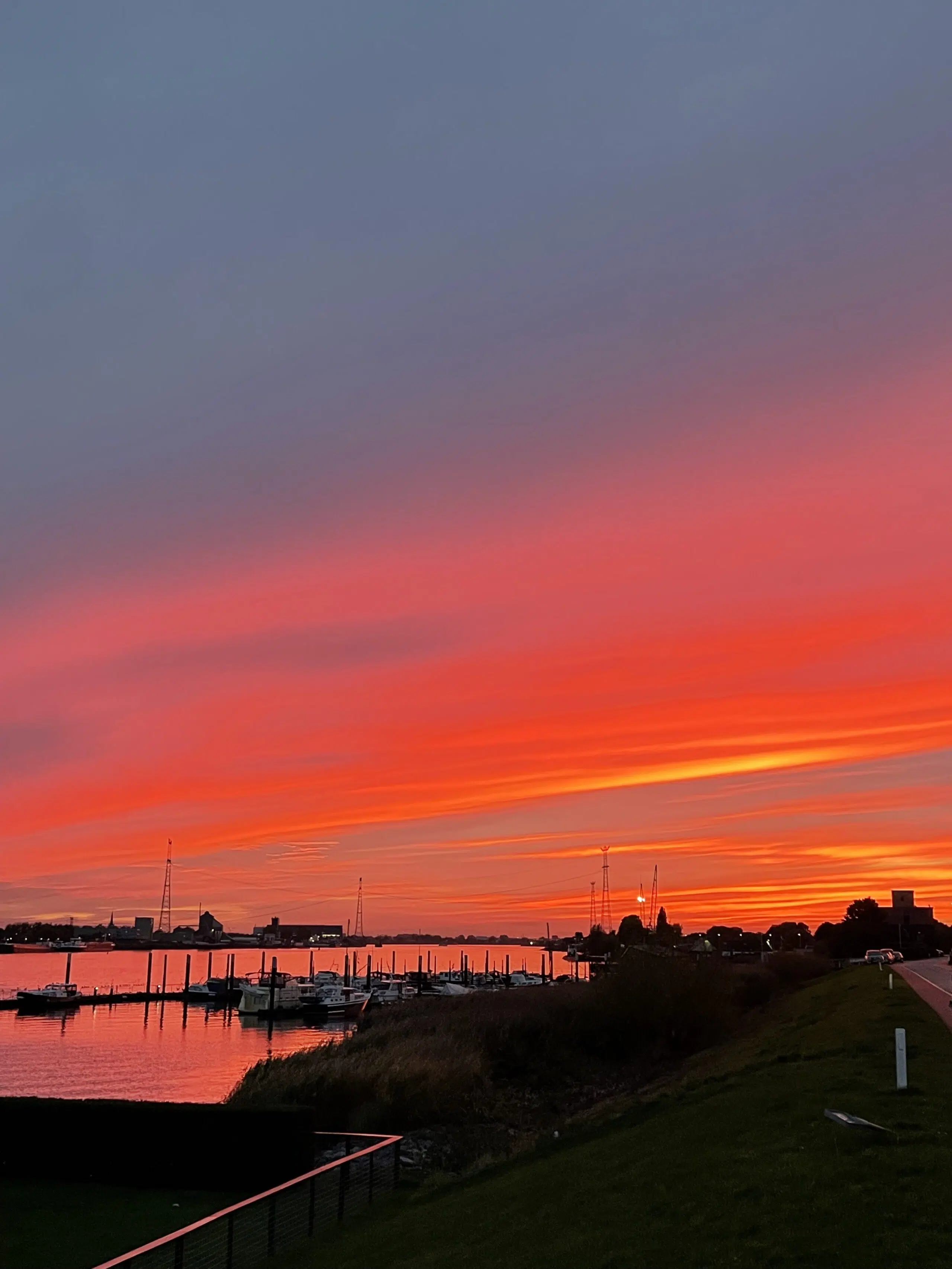 dieprode ondergaande zon boven de boten op de rivier de Lek