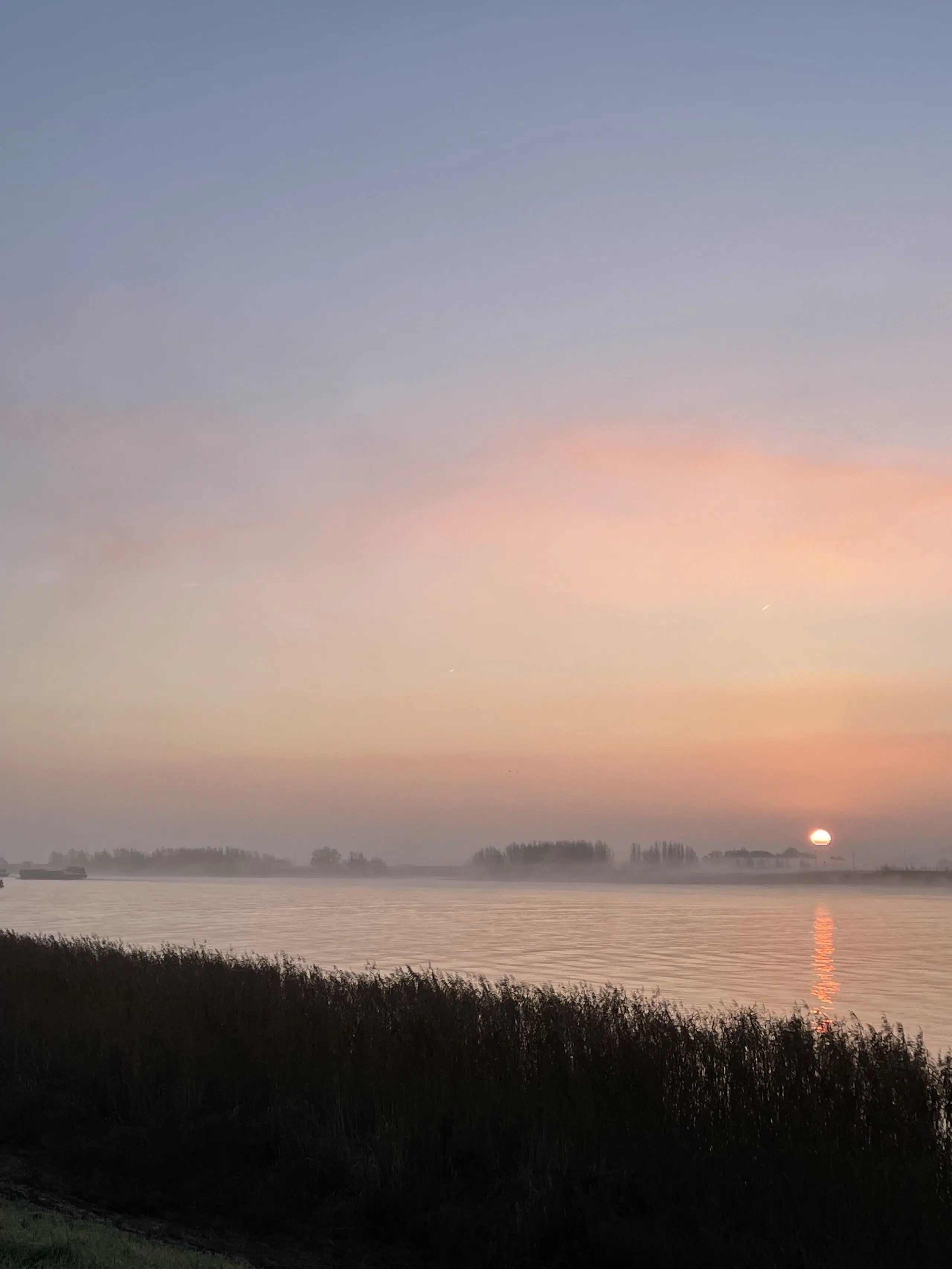 ondergaande zon boven een mistige rivier de Lek