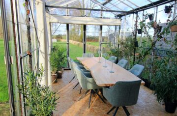 vergadertafel met planten eromheen in een glazen kas met uitzicht op het groen