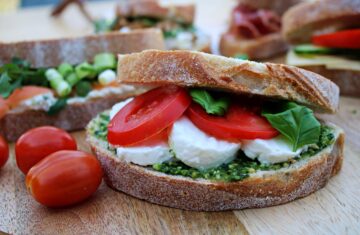 broodje mozzarella tomaat pesto en basilicum met snacktomaatjes op een plank